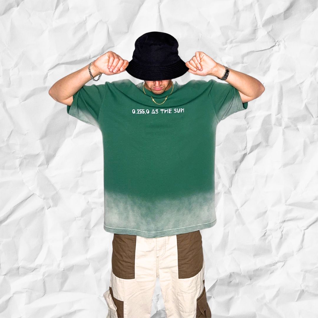 Model lifting arms while wearing Hyperreal Sun Tee by DALTONICO, showcasing the bold white text “0.255.0 AS THE SUN” on a green-to-white faded oversized shirt.