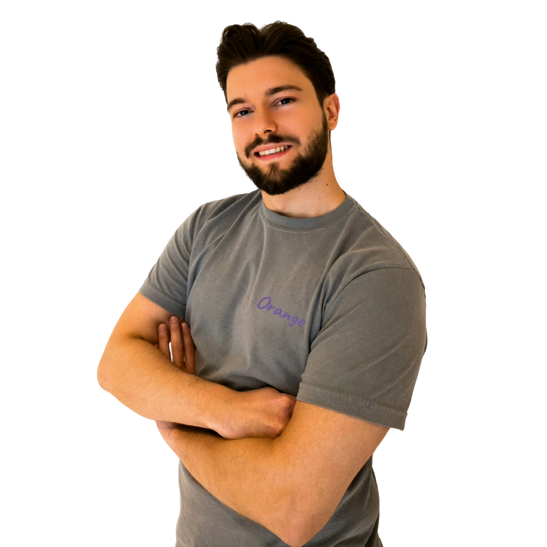 A smiling man wearing a Gray T-shirt with the word 'Orange' embroidered in Purple on the left chest. This casual, premium cotton T-shirt is designed for a comfortable and modern fit, perfect for everyday wear and expressing a unique sense of style. The model stands confidently with arms crossed, showcasing the shirt's relaxed vibe.