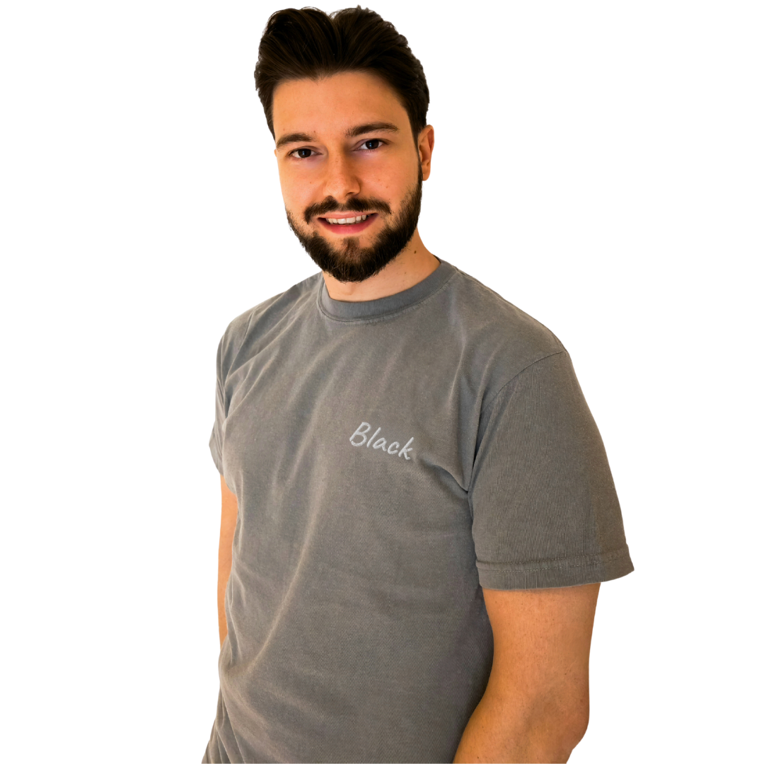 A man wearing a Gray T-shirt with the word 'Black' embroidered in White on the left chest. This premium cotton T-shirt is designed for comfort and casual style, perfect for everyday wear. The model smiles confidently, showcasing the shirt's simple and modern design.