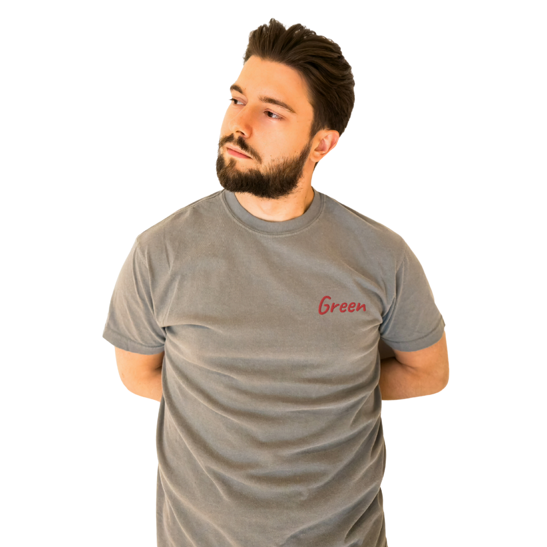 A man wearing a Gray T-shirt with the word 'Green' embroidered in Red on the left chest. The T-shirt is made from premium cotton for a comfortable fit, ideal for everyday wear and casual style. The model is posing with his arms behind his back, looking to the side to highlight the shirt's front design.