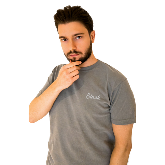 A unisex Gray T-shirt featuring the word 'Black' embroidered in White on the left chest. This premium cotton T-shirt offers a modern fit and is perfect for casual wear or making a bold fashion statement. Styled by a confident model with a thoughtful pose to showcase the shirt’s unique design.